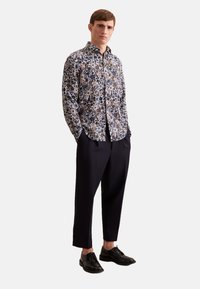 Camicia a fantasia floreale in blu navy, con colletto button-down, maniche lunghe, abbinata a pantaloni scuri su misura e scarpe nere.
