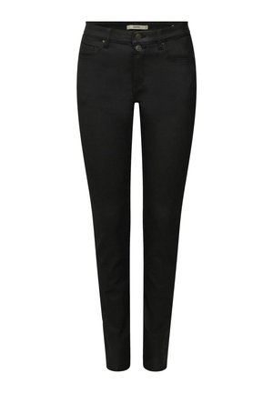 Femme portant un col roulé jaune ajusté, un jean noir slim retroussé aux chevilles et des mocassins noirs brillants, debout devant un fond uni.