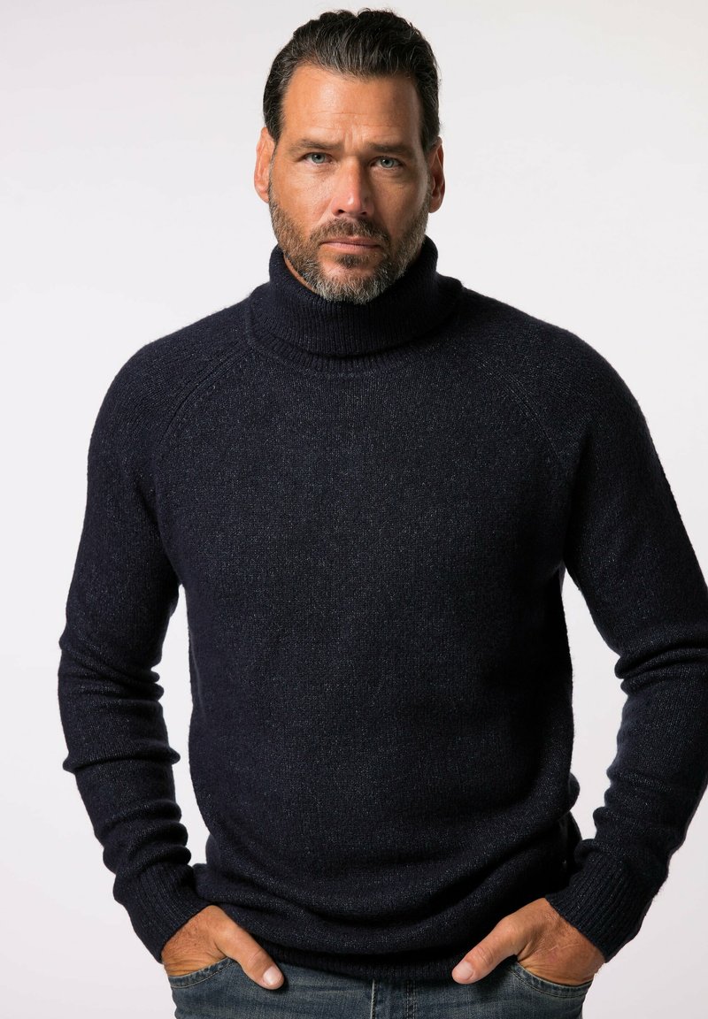Maglione a collo alto di un blu navy scuro, realizzato in un tessuto a maglia testurizzato, con maniche lunghe e un design aderente, indossato sopra dei jeans di denim.