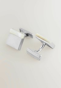 Stříbrné manžetové knoflíčky čtvercového tvaru, s hladkým bílým kamenem jako akcentem. Lesklý povrch, minimalistický design a pevné otočné zavírání.