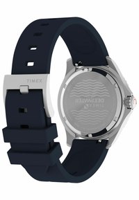 Zegarek Timex z srebrną stalową obudową, granatowym silikonowym paskiem z prostokątnymi wycięciami oraz metalowym zapięciem.