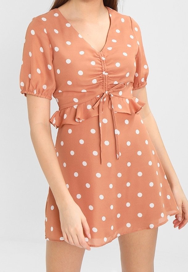 Kurzärmliges, rostfarbiges Kleid mit weißen Punkten, tailliertem Oberteil, V-Ausschnitt, Rüschensaum und Bindedetail an der Taille.