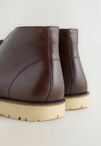 Pair of dark brown leather ankle boots with beige rubber soles, shown from back and slightly angled on a light background.