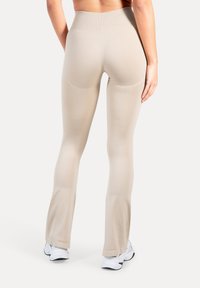 Beige leggings met hoge taille, een gladde textuur en een uitlopende vorm, voorzien van subtiele stikdetails en gecombineerd met witte sportschoenen.