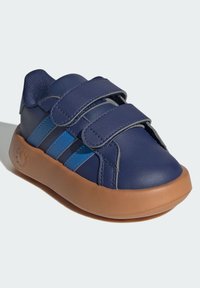 Chaussure en cuir bleu avec des bandes Velcro, présentant un dessus bleu marine foncé, des rayures bleu clair et une semelle en caoutchouc marron. Design à bout arrondi.