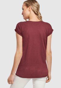 Bordeaux kortærmet t-shirt med rund halsudskæring og opsmøgede ærmer, der har en tekstureret stofkvalitet og en let buet kant.