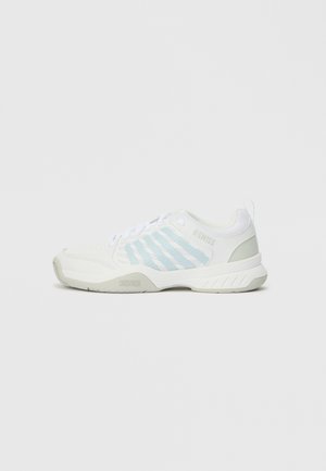 Zapatilla deportiva blanca con rayas azul claro, punta redonda y entresuela texturizada. Cuenta con cordones y una lengüeta trasera para facilitar su uso.