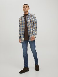 Plaid flannel shirt in blue, beige, and white, worn over a dark brown top. Fitted blue jeans and brown suede ankle boots complete the outfit.