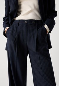Pantaloni a righe navy realizzati in tessuto, con doppie pieghe frontali, tasche laterali e chiusura a doppio bottone. Texture liscia e vestibilità su misura.