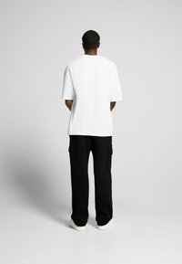 Vit t-shirt med kort ärm och avslappnad passform, kombinerad med löst sittande svarta cargobyxor med sidofickor och vita sneakers.