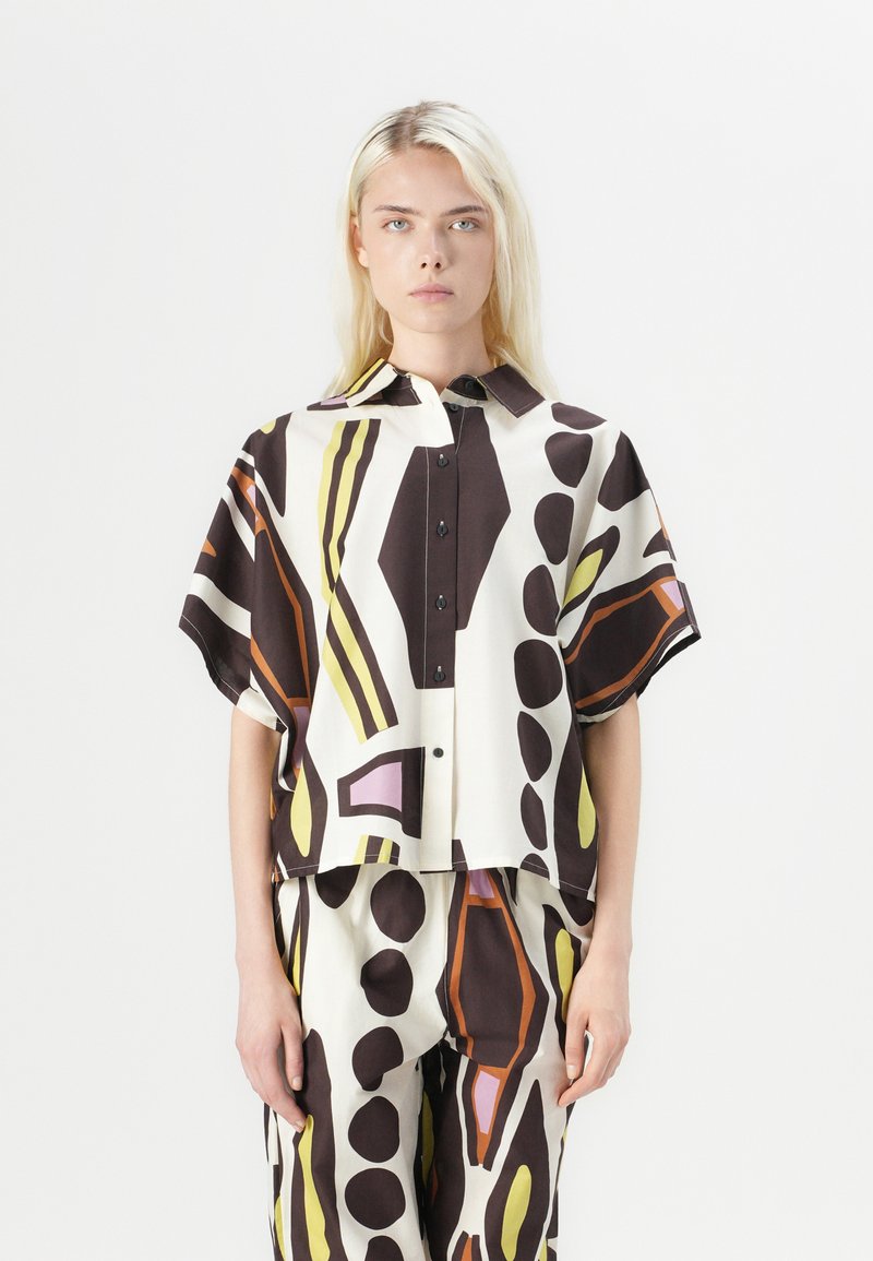 Chemise à manches courtes, col en tissu lisse, présentant un motif abstrait audacieux avec des tons de marron, crème, jaune et des accents violets.