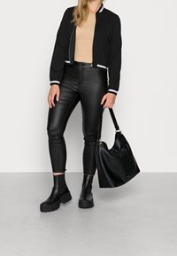 Černá bomber bunda s bílými pruhovanými manžetami, béžový žebrovaný top, černé koženkové kalhoty, černé kotníkové boty a černá kabelka.