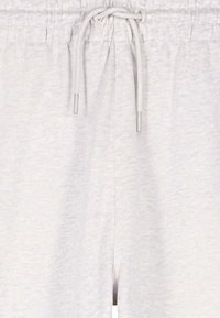 Dettaglio di pantaloni della tuta grigio chiaro che mostra la fascia elastica in vita con coulisse annodata e terminali in metallo.