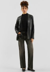 Zwarte leren blazer over een zwarte geribbelde trui, gecombineerd met donkergrijze jeans met wijd uitlopende pijpen. Opvallend detail: ronde tas met studs aan de riem.