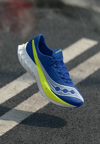 Sapatilha de corrida azul com um upper em malha, detalhes em verde limão e uma sola branca texturizada. Apresenta um padrão de linha ondulada e atacadores planos.