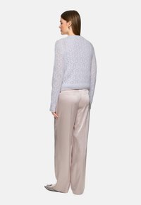 Light purple, knitted sweater with patterned texture and long sleeves, paired with high-waisted, shiny light pink wide-leg trousers.