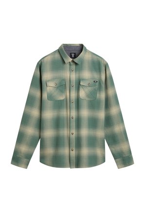 Groen-beige geruite blouse met lange mouwen, twee borstzakken en een kraag, plat neergelegd op een witte achtergrond.