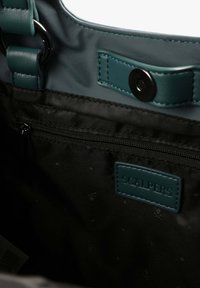 Interno nero di una borsa con una tasca con zip, dettagli in pelle verde acqua e un'etichetta "SCALPERS". Texture liscia e dettagli in metallo.