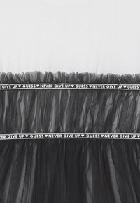 Maglietta bianca con una gonna in tulle nero sottostante, caratterizzata da una texture arricciata e una fascia in vita con la scritta "NEVER GIVE UP" in bianco su sfondo nero.