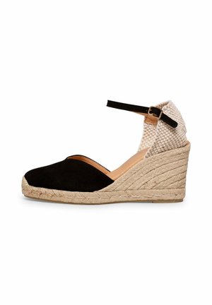 Alpargata cuña con puntera cerrada negra, talón tejido beige, correa en el tobillo con hebilla y suela de cuerda natural.