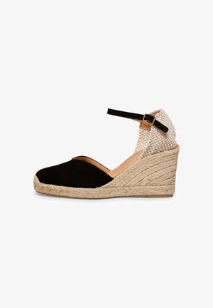 Alpargata cuña con puntera cerrada negra, talón tejido beige, correa en el tobillo con hebilla y suela de cuerda natural.