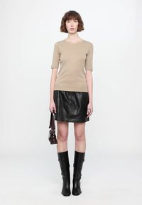 Beige ribbed short-sleeve top, black leather mini skirt, knee-high black boots, and a small dark burgundy handbag. Clean, fitted silhouette.