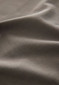 Textúrovaná látka v tlmenej hnedej farbe, s jemným vzorom tkania, vykazujúca mäkké, mierne zvrásnené záhyby.