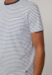 Camiseta de manga corta a rayas en blanco y marino, con bolsillo en el pecho, cuello redondo con borde marino y un pequeño logo de acento en el dobladillo.