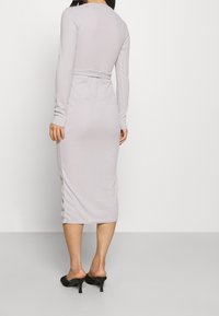 Langärmliges, figurbetontes Kleid aus hell-lila Stoff mit glatter Textur, mittellang bis zur Wade und einem Taillendetail mit Bindeband.