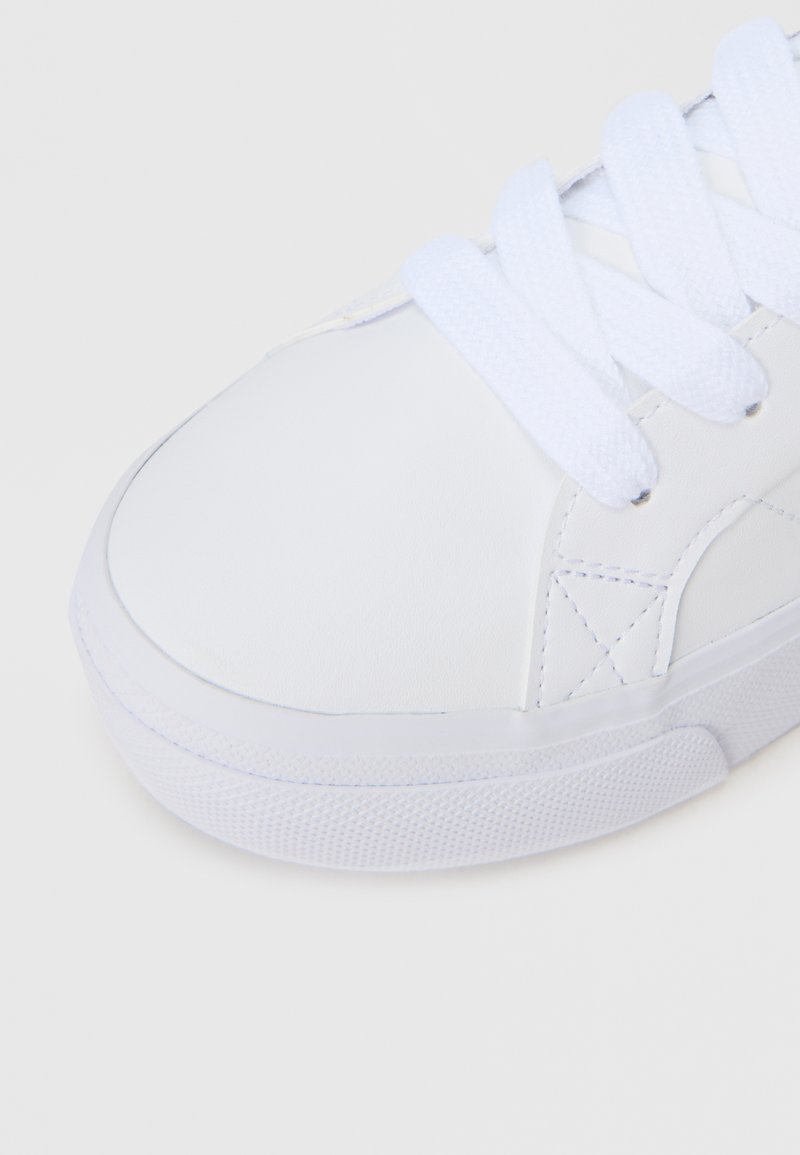 Hvid lædersneaker med flade hvide snørebånd, rund tå, tekstureret gummisål og minimale syningsdetaljer på overdelen.