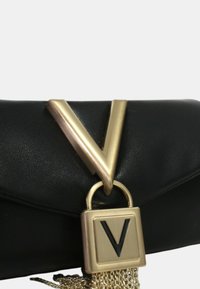 Clutch in pelle nera con un accento a forma di V dorata e un frangia in catena dorata. Include una chiusura quadrata con un dettaglio a forma di V nera.