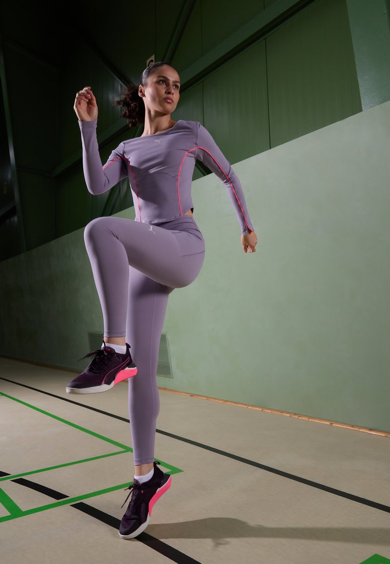 Šviesiai purpurinė sportinė palaidinė ir leggingai su rožin�ėmis akcentais. Sportsiniai bateliai turi juodą pagrindą su rožiniu padu. Vidinė sporto salė su žaliais sienomis.
