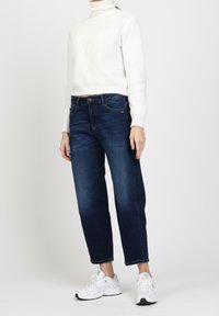 Donker denim jeans met een relaxte pasvorm en rechte pijpen, gecombineerd met een witte gebreide coltrui en witte sportschoenen.