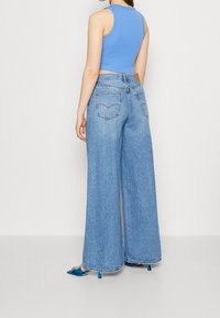 Top court bleu clair et jean en denim à jambes larges. Le jean présente un délavage classique, cinq poches et un ourlet droit.