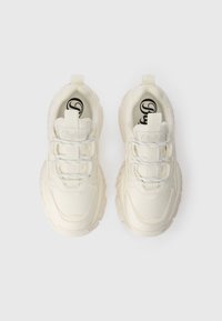 Baltas sporta apavu pāris ar teksturētu virsu, izceļoties ar ievērojamiem šņorēm, mīkstu zoli un zīmola logotipu uz mēles un papēža cilpas.