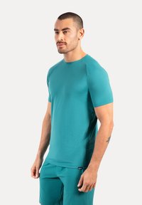 Turkusowa koszulka sportowa wykonana z lekkiego, elastycznego materiału. Posiada krótkie rękawy i okrągły dekolt. Gładka struktura, minimalne oznakowanie.