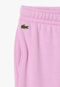 Pantalons de survêtement roses en tissu doux, avec une taille élastique et des poches latérales. Un petit logo de crocodile vert est brodé sur la gauche.