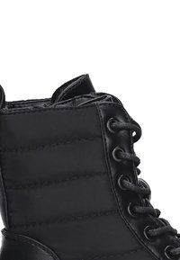 Botín negro de tobillo hecho de cuero suave con textura acolchada, que presenta ojales de metal y cordones para el cierre.