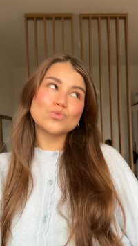 Cardigan gris clair avec bords à volants et boutons, porté par une personne aux longs cheveux bruns dans un décor neutre avec des accents en bois.