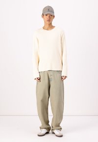 Suéter de canalé crema, pantalones sueltos verde pálido, gorra gris, zapatillas blancas con detalles en marrón. Ajuste simple y relajado con un mínimo de detalles.