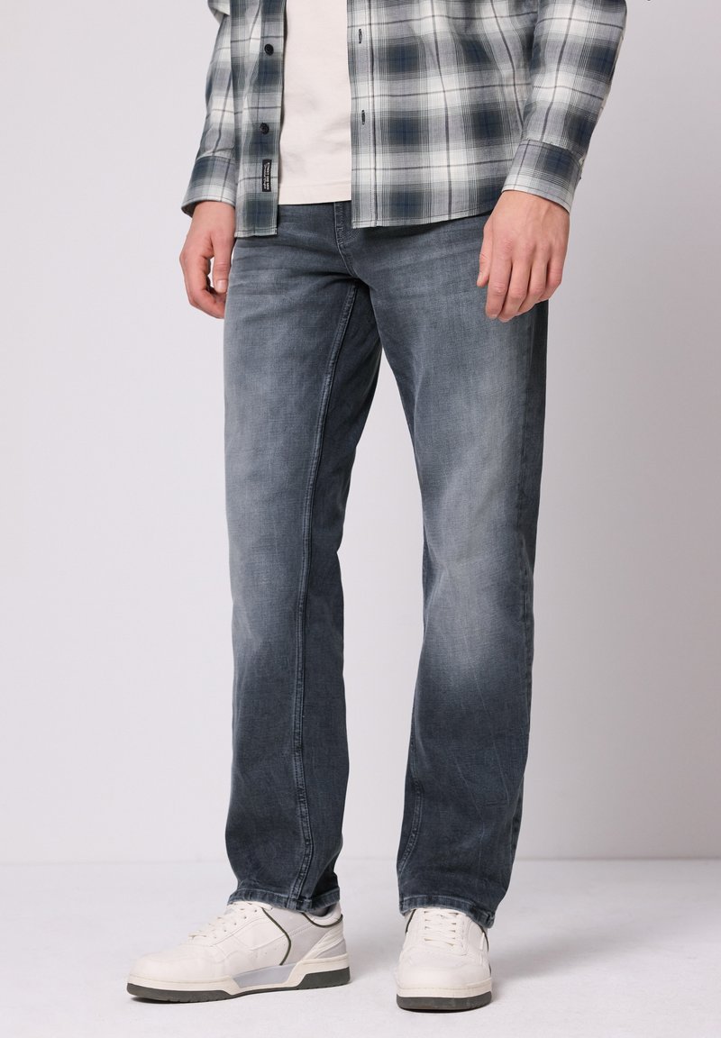 Jean bleu foncé avec une finition délavée, coupe droite, style cinq poches, associé à des baskets blanches et une chemise à carreaux.