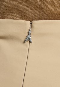 Îmbrăcăminte bej cu o textură netedă, având un top tricotat maro și un fermoar în formă de insectă de culoare argintie ca detaliu notabil.