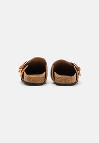 Sandales en daim marron avec boucle latérale adjustable, semelle en liège et semelle en caoutchouc noir texturé, vues de l'arrière.
