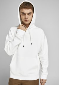 Witte hoodie met een voorzak, koorden en geribde mouwen. Model heeft lichtbruin haar en draagt een zilveren ring.