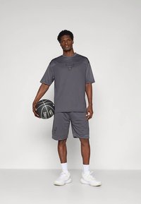 Grå treningstøy-sett med kortermet skjorte og shorts med preget logo; inkluderer en basketball, brukt med hvite sko.