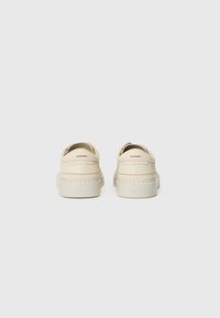 Chaussures en cuir beige avec une finition texturée, de forme arrondie et un design minimaliste. Présentent une semelle blanche épurée et un branding subtil.