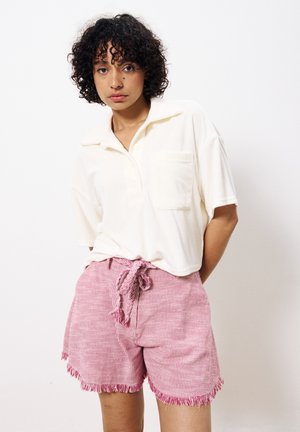 Hellblaustes, kurzärmeliges Poloshirt mit einer Tasche, kombiniert mit rosa gestreiften, ausgefransten Shorts mit einem Kordelzugbund.