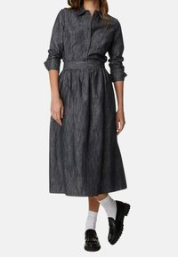 Czarna sukienka koszulowa z ciemnego denimu, z zapięciem na guziki z przodu, długimi rękawami, paskiem w talii i zwiewnym, średniej długości dołem. Stylizowana z czarnymi mokasynami i białymi skarpetkami.