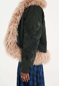Giacca bomber verde oliva con un morbido colletto in pelliccia sintetica rosa. Presenta un intricato ricamo nero di un uccello sulla manica. Polsini a coste.
