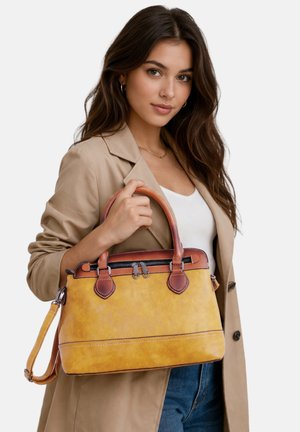 Vrouw in beige blazer houdt grote gele en bruine leren handtas met handgrepen en schouderriem vast, draagt witte top en blauwe spijkerbroek.